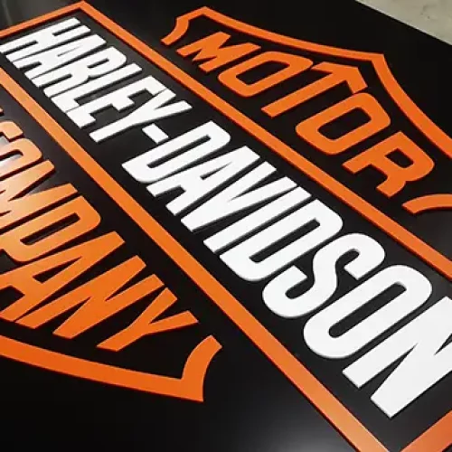 Logo Harley-Davidson comportant les mots Motor and Company en orange et Harley-Davidson en blanc, sur fond noir. Le texte est disposé à l'intérieur de deux boucliers aux contours orange, idéaux pour un travail de précision avec un laser découpeur.