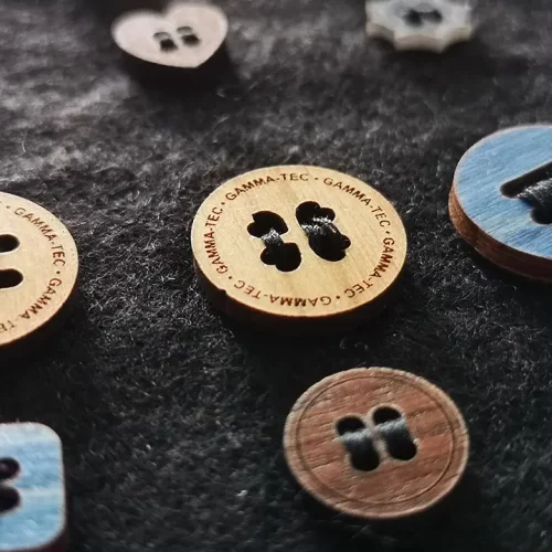 Gros plan sur divers boutons en bois posés sur une surface en tissu sombre. Les boutons sont de formes, de tailles et de couleurs différentes, et certains comportent un texte gravé sur le pourtour.